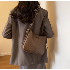 Close-up of brown leather bucket bag featuring a woven ethnic style wide shoulder strap