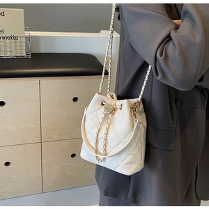 Close-up of beige quilted bucket bag with leather drawstring and metal chain strap