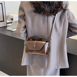 Brown glossy small square bag styled with grey suit in a modern minimalist interior