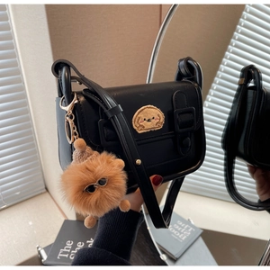 Détail du sac bandoulière noir avec écusson et breloque pompon marron sur fond vintage