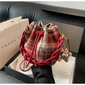 Détail d'un sac seau à carreaux rouge et gris avec poignée en cuir tressé en boîte