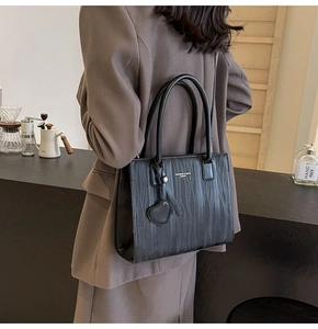 Détail du sac cabas noir avec texture ondulée verticale et breloque en cuir en cœur