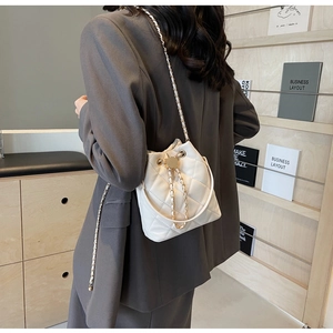 Detail shot of white quilted bucket bag with golden chain strap and drawstring closure