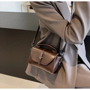 Detail of dark brown vintage crossbody bag with metal buckle worn with grey blazer