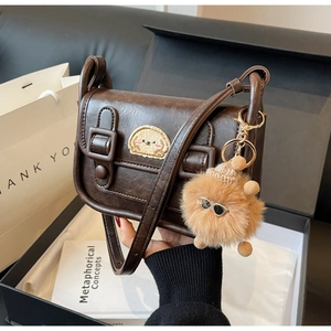 Détail du sac à bandoulière en cuir marron foncé avec broderie chien et porte-clé peluche