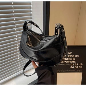 Detail of black glossy patent leather crossbody bag with silver eyelet strap and hardware