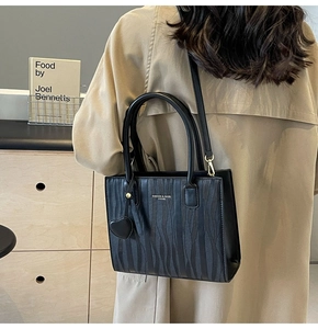 Détail du sac à main noir à texture ondulée avec breloque cœur et logo imprimé