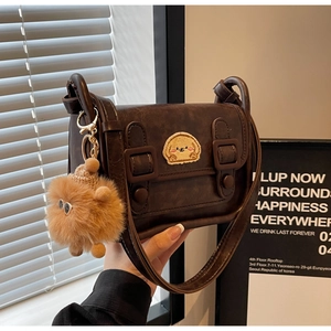 Détail du sac bandoulière vintage marron avec écusson chiot et breloque peluche