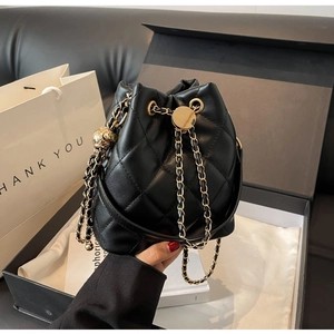 Close-up of black quilted bucket bag with gold chain strap and metal ball fastener