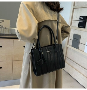 Sac à main noir en cuir texturé avec détails dorés porté par un mannequin en trench-coat