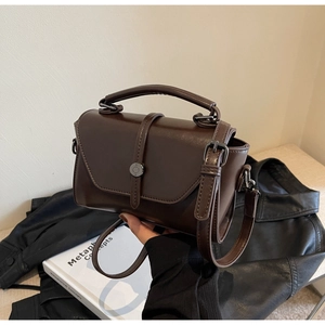 Detail view of a vintage dark brown leather crossbody bag with metal buckle on a black jacket