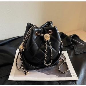 Detailed view of black quilted bucket bag with gold chain strap and metal drawstring ball