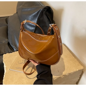 Detail of caramel patent leather shoulder bag with dual zippers and eyelet strap