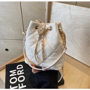 Close-up of quilted white bucket bag with drawstring closure and gold chain strap