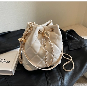 Detail of cream quilted bucket bag with gold chain strap and drawstring closure
