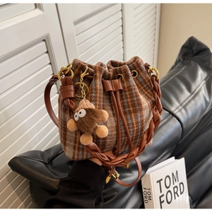 Détail d'un sac seau vintage en laine à carreaux avec anse en cuir et breloque ourson