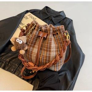 Détail du sac seau à carreaux avec anse tissée et breloque peluche sur cuir