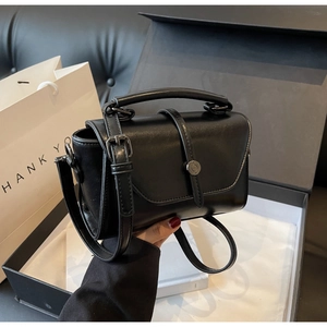 Detail of black faux leather handbag with silver metal buckle and top handle in gift box