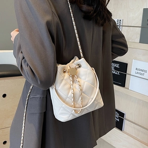 White quilted bucket bag with gold chain strap shown on a model in a cozy setting
