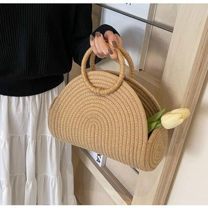 Detail of a semi-circular straw woven handbag with round handles and a tulip decoration