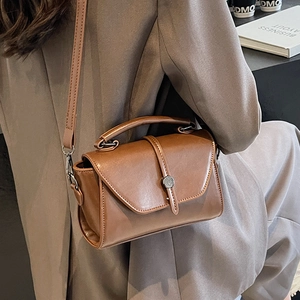 Brown vintage leather crossbody bag with top handle and metal buckle shown in a lifestyle setting