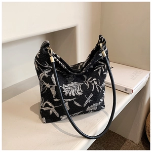 Detail of black woven bucket bag with white tropical leaf prints and gold-tone hardware