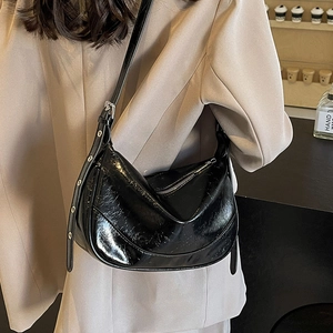 Glossy black leather half-moon crossbody bag with silver buckle worn by a model