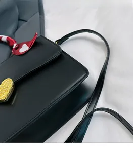 Détail d'un sac à main en cuir noir avec fermoir cœur doré et foulard en soie décoratif