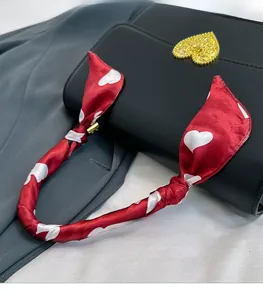 Détail d'une poignée de sac en cuir noir avec foulard en soie rouge à motifs de cœurs