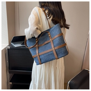 Detail of denim tote bag with brown faux leather straps and gold rivets worn by a model