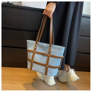 Detail of denim tote bag featuring brown leather cross straps and gold metal rivet accents