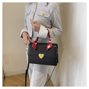Détail du sac à main en cuir noir avec boucle cœur dorée et foulard en soie rouge imprimé