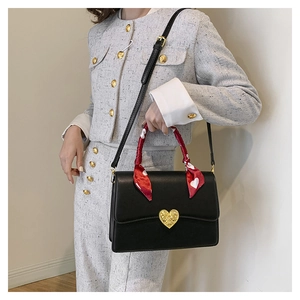 Détail du sac à main en cuir noir avec boucle cœur dorée et foulard en soie rouge