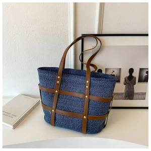 Detail of blue denim tote bag with brown faux leather trim and gold rivet accents