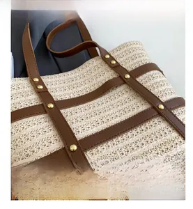 Detail of beige woven tote bag with brown leather straps and gold metal rivet accents