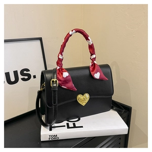 Détail du sac à main en cuir noir avec fermoir cœur doré et poignée décorée d'un foulard
