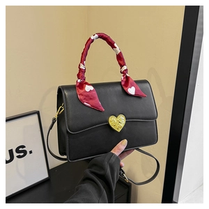 Détail du sac en cuir noir avec fermoir cœur doré et poignée ornée d'un foulard en soie rouge