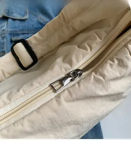 Detail showing smooth silver metal zipper pull and cream quilted nylon bag fabric