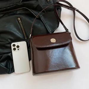 Detail van bordeauxrode laklederen tas met gouden ronde sluiting en verfijnde textuur