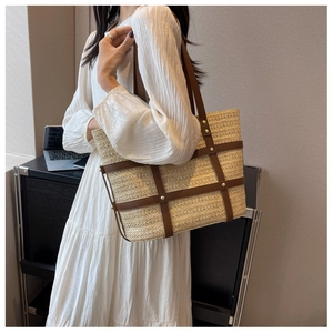 Detail of woven straw tote bag with brown leather cage frame and gold studs decoration
