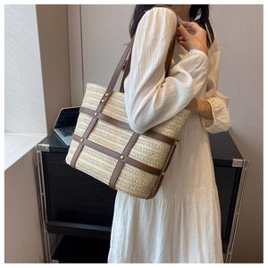 Detail of woven straw tote bag featuring brown leather cross-straps and gold rivet accents