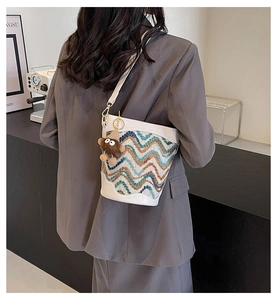 Detail of a textured wave-pattern bucket bag with a plush charm on a white leather strap
