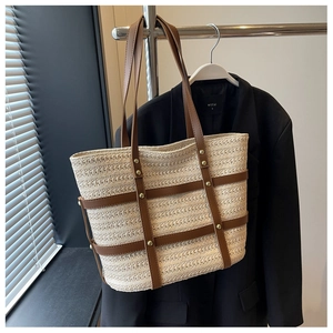 Detail of woven tote bag featuring brown leather handles and decorative gold rivets