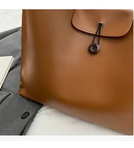 Detail of a brown leather tote bag showing soft texture and unique wooden button closure