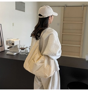 Detail of a large off-white nylon tote bag with side pocket in a minimalist cafe setting
