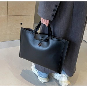 Detail view of a black matte leather tote bag with button closure and dual handle straps
