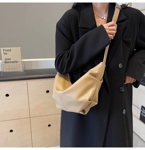 Dettaglio della borsa a pieghe beige indossata con un blazer nero in stile minimal