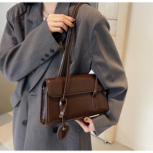 Detail of glossy brown underarm bag with double straps and flap closure on gray blazer