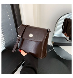 Detail van een donker koffiebruine crossbodytas van kunstleer met metalen logo en zilveren gesp