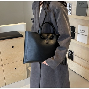 Detail of minimalist black leather tote bag with unique wood button closure and spacious interior